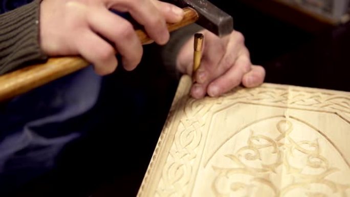 一位工匠坐在他的工作场所，在双陆棋上雕刻木制装饰品。一名男子使用小木棍和锤子处理细节的特写镜头