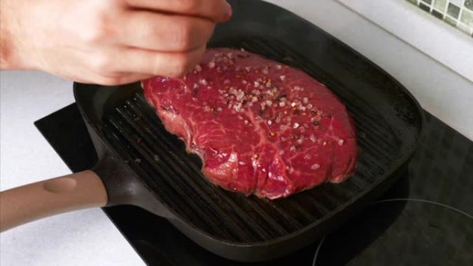 男人的慢动作手在烤盘上的烤牛肉牛排上撒盐