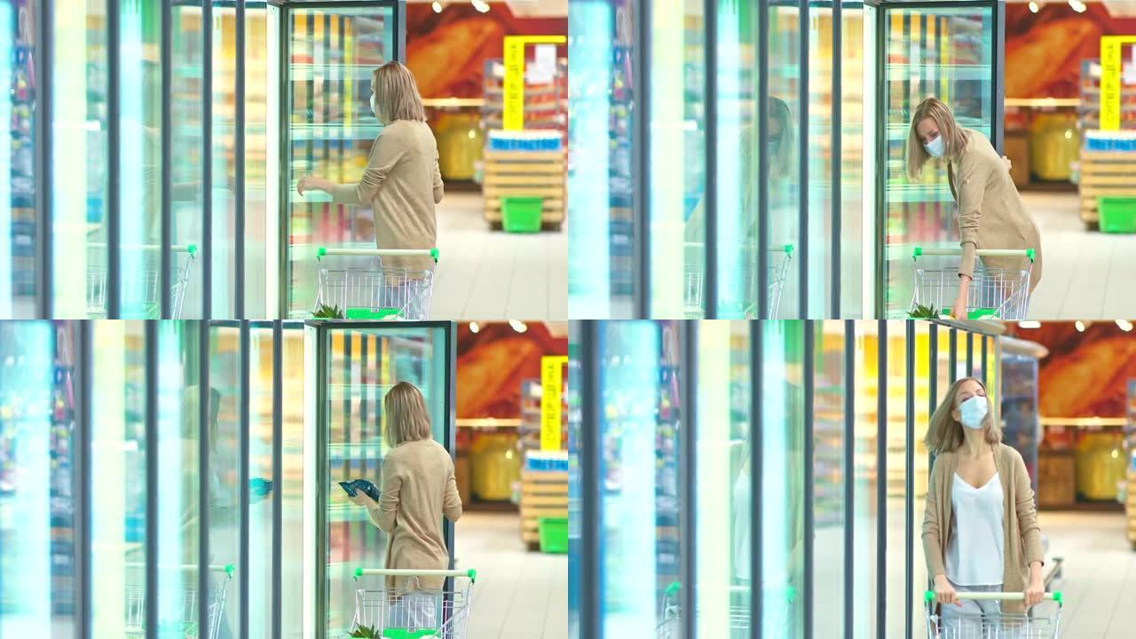 戴着医用防护口罩的年轻女子带着杂货店推车走到超市的冰箱。在检疫期间购买冷冻食品，冠状病毒，新型冠状病