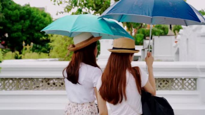 泰国日本同胞的女导游参观该国的主要景点。泰国曼谷的 “Wat Pho” 地标。两名亚洲妇女在雨天撑伞