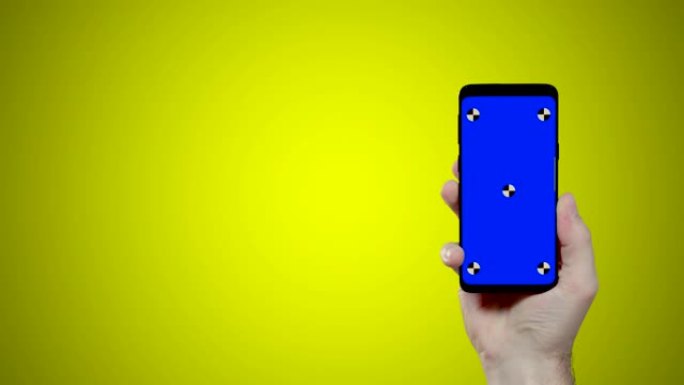黄色背景上带有蓝色croma关键跟踪点的男子手持智能手机进入屏幕右侧