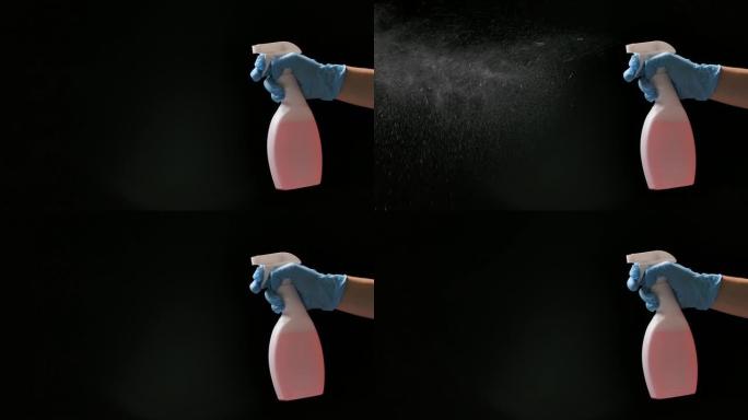 一名戴着防护手套的男子喷洒清洁卫生喷雾剂，以消毒和预防COVID 19。黑色背景上的精细飞溅，慢动作