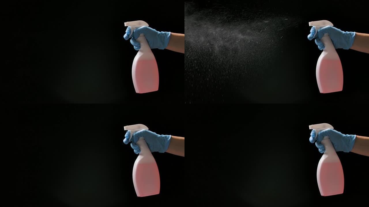 一名戴着防护手套的男子喷洒清洁卫生喷雾剂，以消毒和预防COVID 19。黑色背景上的精细飞溅，慢动作