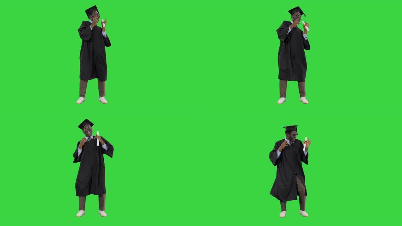 兴奋的非裔美国男学生穿着毕业长袍，在绿屏上与他的文凭快乐地跳舞，色键