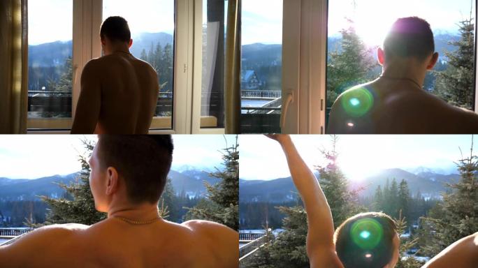 冬天，年轻人在酒店的卧室里揭开窗帘，打开窗户，在阳台上走。运动的家伙早上举手伸展身体。美丽的自然景观