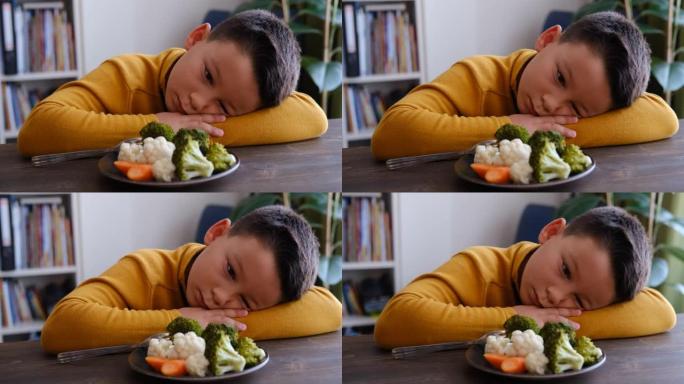 孩子对不得不吃蔬菜非常不满。他的盘子里有很多蔬菜。他讨厌蔬菜。