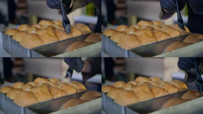 面包店、厨师、戴手套的康迪特女人用硅胶糕点刷润滑烤箱里取出的热香包，特写