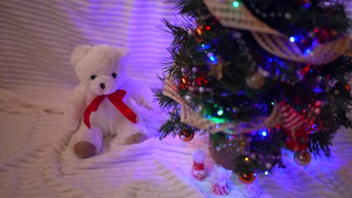 闪亮的圣诞树，在黑暗中有五颜六色的球和玩具。小白泰迪熊坐在圣诞树下，庆祝心情和童话概念