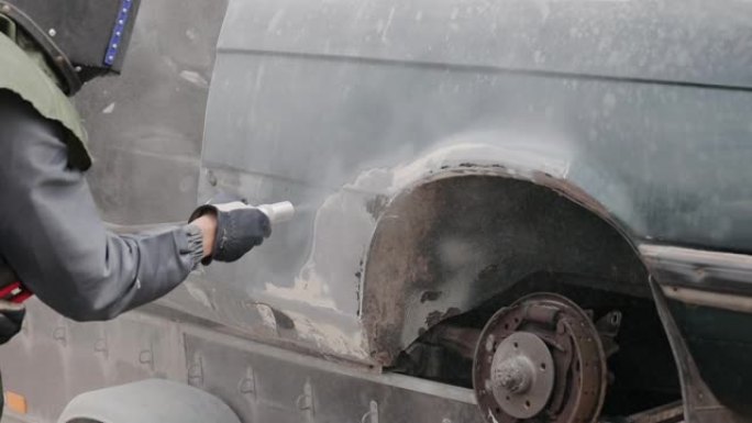工业工人用喷砂枪清洁生锈汽车的金属表面