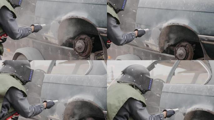 工业工人用喷砂枪清洁生锈汽车的金属表面