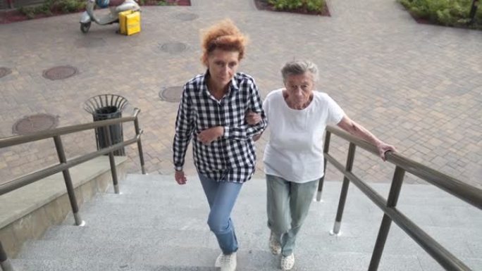 家庭护理员帮助残疾妇女下楼。护士帮助一名高级妇女在楼梯上行走。护理人员帮助退休人员在外面的楼梯上。为