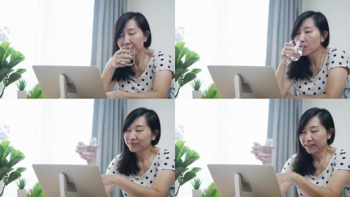 亚洲妇女在新型冠状病毒肺炎期间在家工作时喝一杯水。