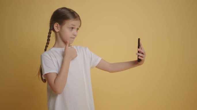 带辫子的女孩在黄色墙壁背景下在手机上自拍慢动作