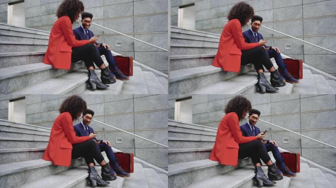 年轻的商务夫妇坐在市区的楼梯上使用智能手机