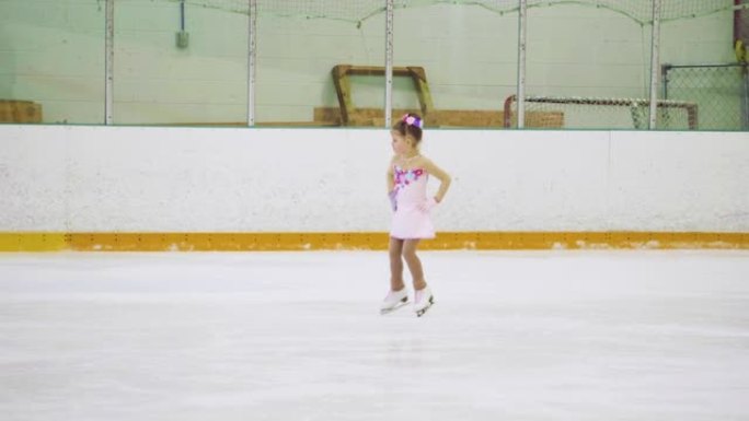 小女孩穿着粉色连衣裙练习花样滑冰元素