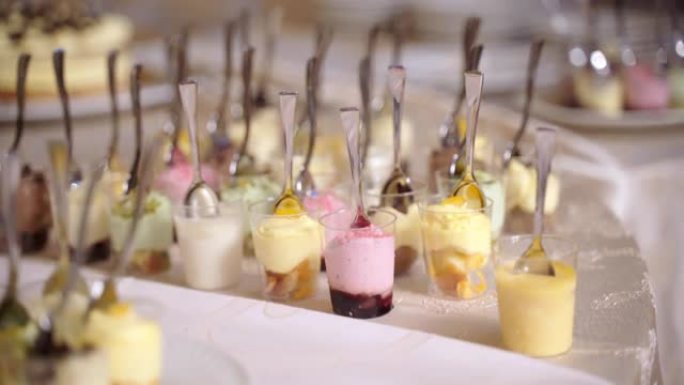 装饰精美的餐饮宴会桌，配有装满果冻小吃，冰淇淋和各种水果的小玻璃酒杯。自助柜台内有茶匙的彩色甜点杯，