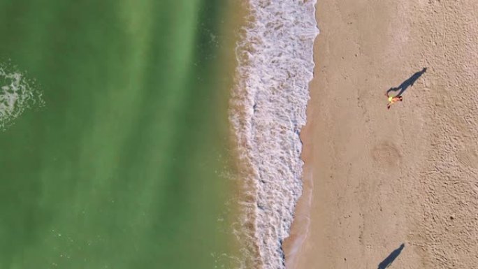 空中自上而下的镜头空着海岸，早上在沙滩上靠海水奔跑