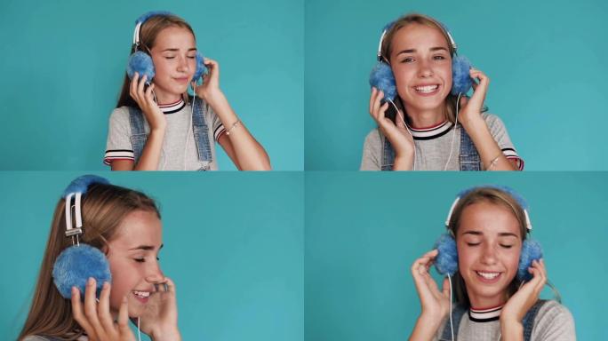 可爱的微笑女孩戴着蓝色大耳机在工作室里听音乐。把手放在耳机上。可爱的少女通过蓝色背景上的耳机听音乐