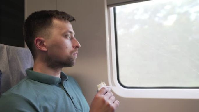 高加索男性旅行者乘坐旅客高速列车在靠窗座位上旅行，吃快餐三明治卷。铁路车厢内部。一个人独自坐火车旅行