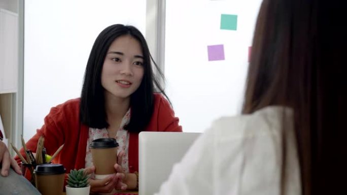 年轻的亚洲女商人坐在办公室，开会，与同事交谈，决心，带着幸福的微笑和从领导那里学习的经验。概念积极思