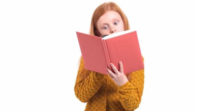 儿童好奇心和教育的概念。可爱的小女孩，留着红色长发，通过放大镜看书。孤立，在白色背景上