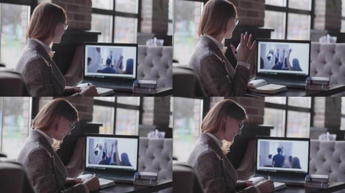 在线培训，这位女企业家正在远程培训高级培训，举起她的手，在咖啡馆wifi的桌子旁坐在笔记本上写字