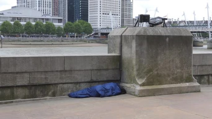 一个无家可归的人睡在泰晤士河畔的照片。