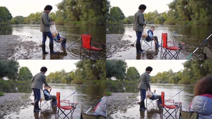 快乐的小家庭一边钓鱼一边享受小吃。坐在河里的钓鱼椅上，鱼竿在水中