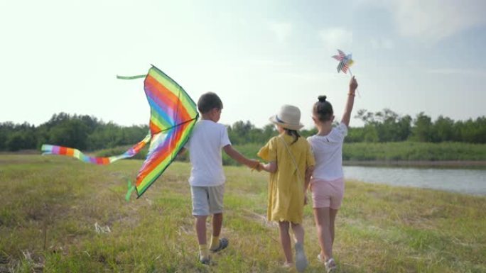 活跃的周末，快乐的孩子朋友在周末在乡村的湖水和芦苇背景下去草地玩风筝