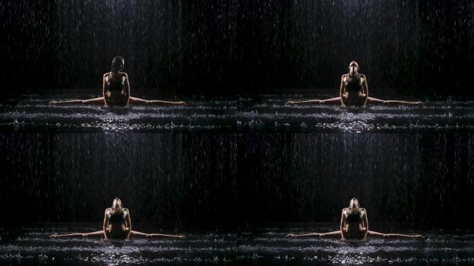 在雨水的溪流下，一个年轻的女人坐在麻绳上，享受锻炼。Studio light在水面上产生微光。慢动作