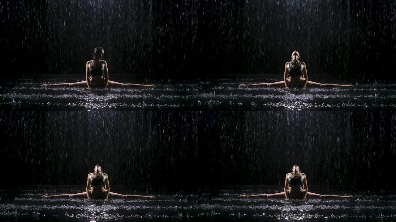在雨水的溪流下，一个年轻的女人坐在麻绳上，享受锻炼。Studio light在水面上产生微光。慢动作