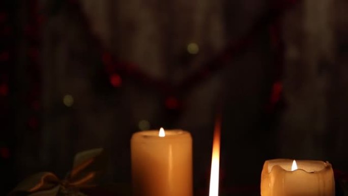 圣诞气氛: 三根点燃的蜡烛，一根在前景中有大火焰，红色和金色的球，剪纸球，缎面金丝带，在低光下从上到