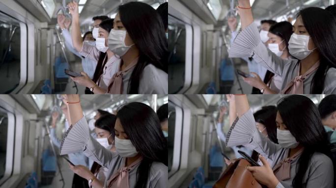 戴口罩的女人使用智能手机设备，站在地铁地铁上，人们乘坐公共交通工具。概念新的正常生活与大流行性流感电