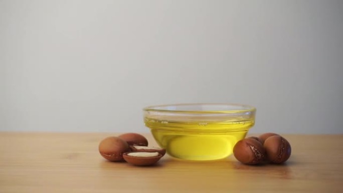将摩洛哥坚果油放入玻璃碗中，并在白色背景上撒上摩洛哥坚果籽。基于摩洛哥坚果油的化妆品概念。
