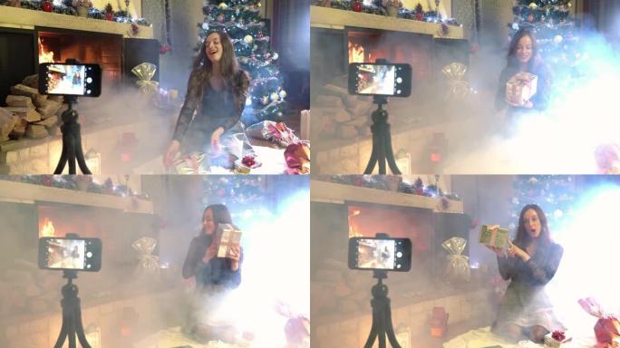 燃烧的壁炉和发光的圣诞树令人惊叹的圣诞气氛，漂亮女人为她的个人博客录制赠送视频，为带有粉色丝带的彩票