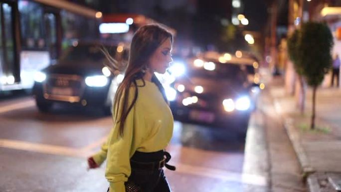 在城市夜生活中，漂亮女孩在夜间穿越街道的城市行走
