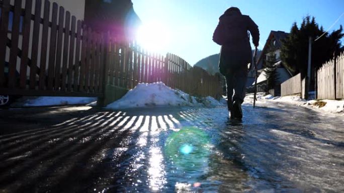年轻的徒步旅行者在郊区的冰道上行走。晴天，无法识别的背着背包的家伙在旅途中走上冰冷的道路。寒假或假期