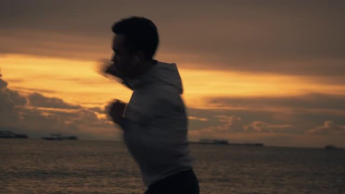 一个亚洲拳击手的剪影在夏天美丽的日落时在海滩上练习拳击锻炼。