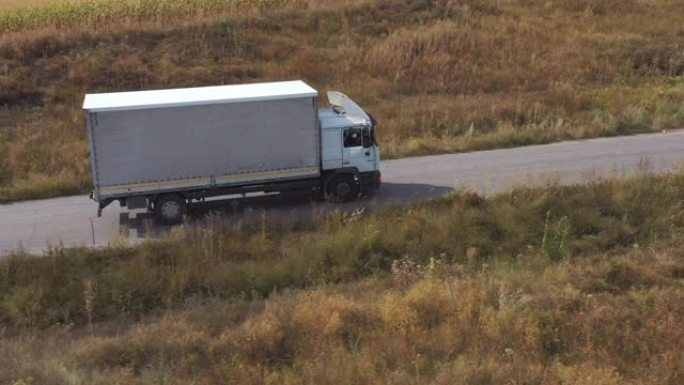 载货拖车在公路上行驶并运输货物的卡车的航拍。飞越送货卡车，沿着高速公路驶过农村的田野。风景优美的自然