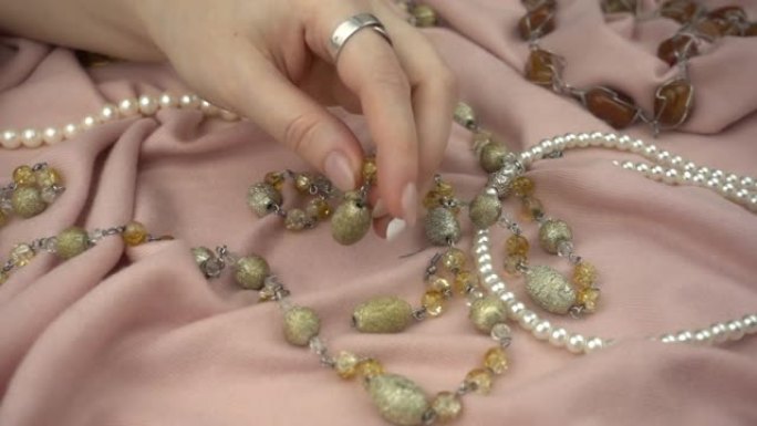 女人的手在慢动作中选择珠宝。在柔和的粉红色柔软织物上特写不同的珠宝。