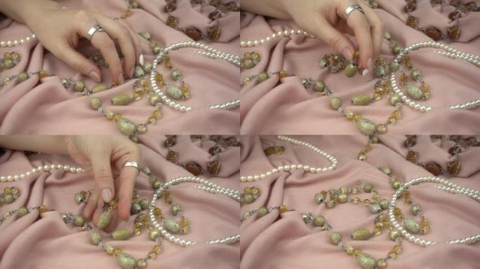 女人的手在慢动作中选择珠宝。在柔和的粉红色柔软织物上特写不同的珠宝。