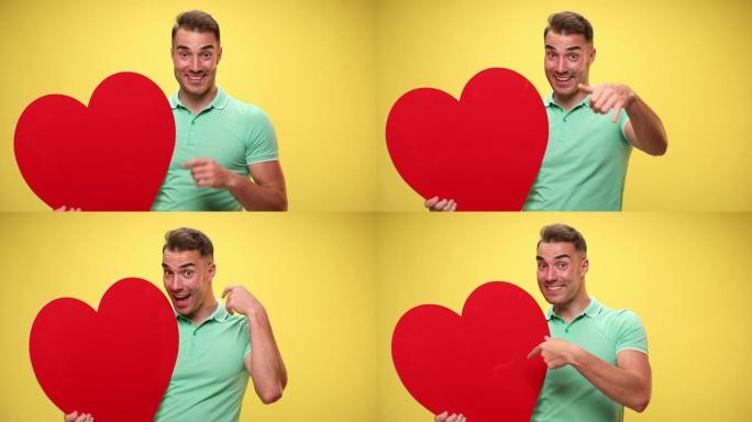性感的休闲男人抱着一颗红色的大心脏，指着相机，指着一个叫我的标志，指着黄色背景上的心脏