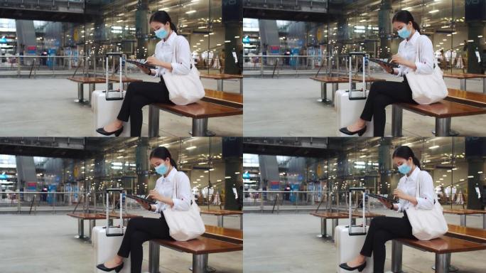 迷人的女商人戴着外科口罩在平板电脑上工作，坐在机场航站楼的椅子上检查电子邮件，并在新型冠状病毒肺炎大