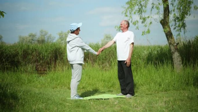 开朗的已婚老年夫妇照顾自己的健康，在阳光明媚的早晨，在绿草和天空的自然背景下，在瑜伽垫上进行体育锻炼
