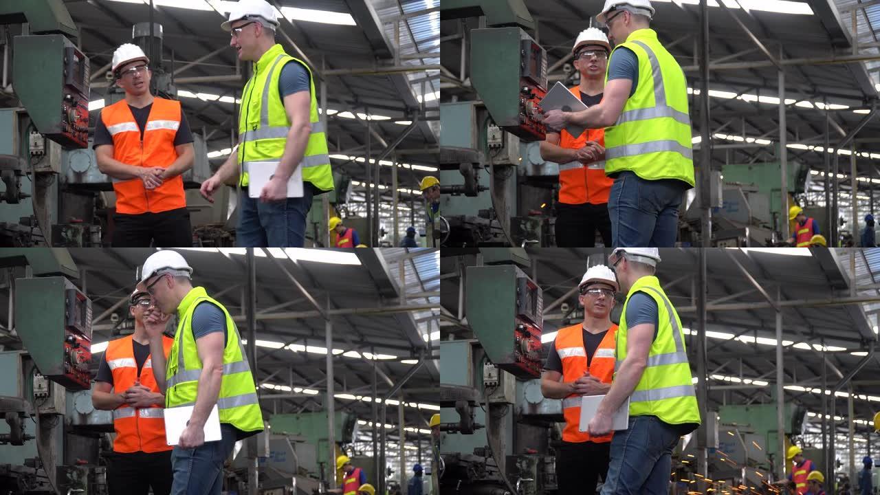 当工人在工业工厂工作时，戴着安全帽的工程师和检查员经理一起交谈，并用平板电脑检查机器。