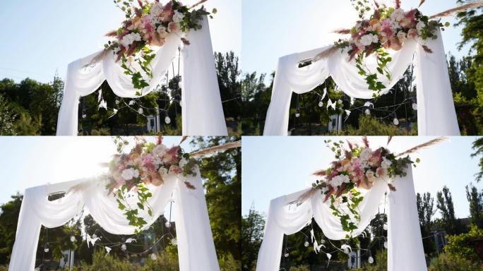 阳光明媚的夏日用鲜花装饰的婚礼拱门。节日花卉装饰。玫瑰和羽毛草，白色纺织框架上有灯泡花环