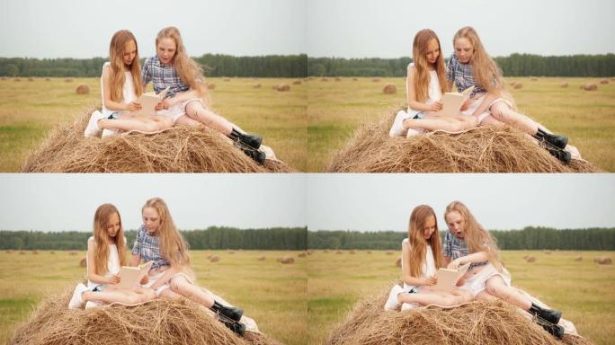 度假时，十几岁的女孩在乡下的草堆上看书。惊讶的女孩在村庄的收割田里看着干草堆上的书。
