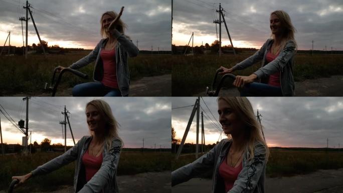 日落时分，金发女郎在草地上骑自行车。农村