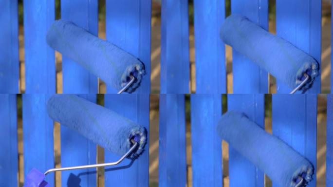 用亮蓝色染料关闭沿木栅栏滚动的油漆滚筒。房屋装饰工作概念。户外
