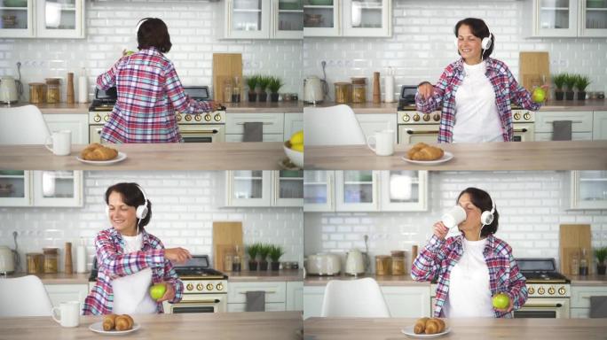快乐的美国老年家庭主妇在现代厨房用耳机跳舞